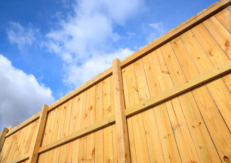 Wooden privacy fence against blue sky with clouds.